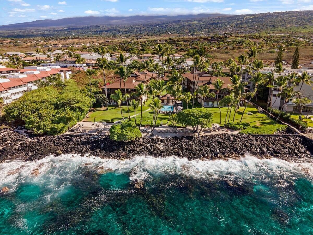 A coastal resort with ocean views, a rocky shoreline, and a well-maintained lawn with palm trees.
