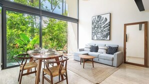 Ein modernes Wohnzimmer mit Essbereich, großen Fenstern, einem grauen Sofa und einem schwarz-weißen abstrakten Gemälde.