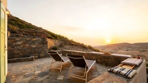A patio with stone flooring, two lounge chairs, a cushioned bench, and a stone wall. - Casa Thymus , great sea view (Agios Charalampos)