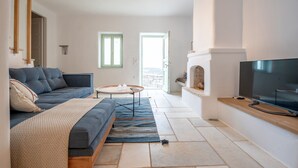 A modern living room with a sofa, a coffee table, and a TV. There is a fireplace and a view of the outdoors. - Casa Thymus , great sea view (Agios Charalampos)