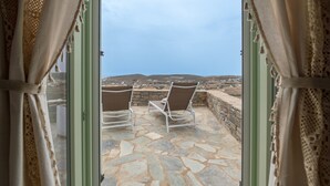 An open doorway leading to a stone patio with two chairs facing a scenic view of hills and a distant town. - Casa Thymus , great sea view (Agios Charalampos)