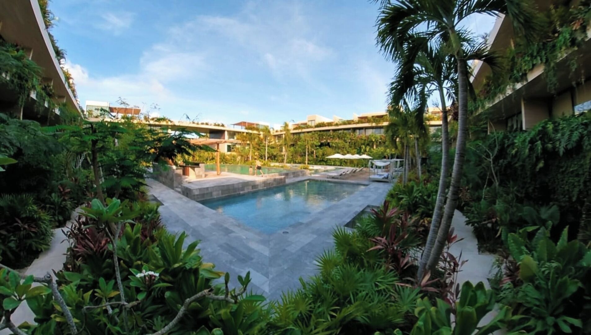Ein Pool, umgeben von üppiger Vegetation und modernen Gebäuden.
