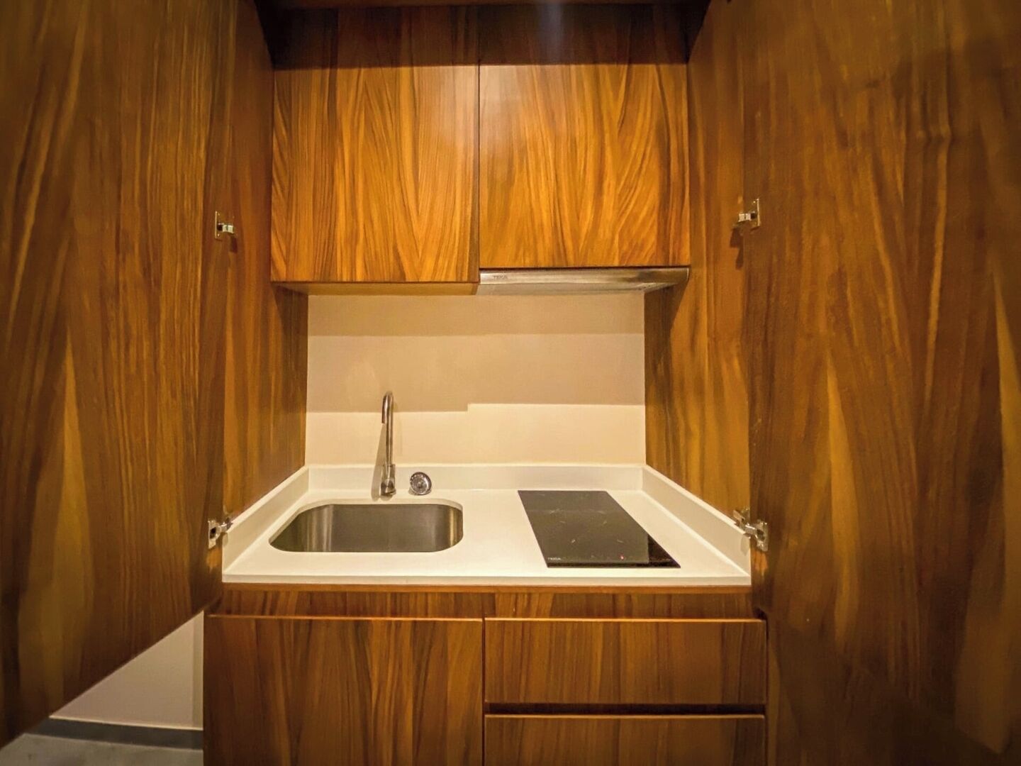 A compact kitchen with wooden cabinetry, a stainless steel sink, and a black countertop.