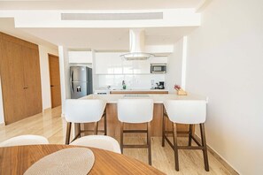 A modern kitchen with a central island, white bar stools, and a dining table with a woven placemat. - Amazing PH, private pool. ocean view, AC and Wi-Fi (Cabo San Lucas)