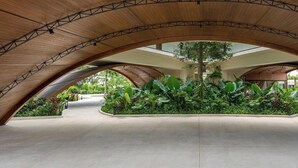Amplo espaço interno com teto de madeira curvo e um jardim central com diversas plantas.