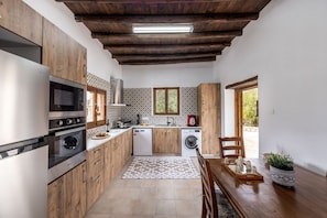 A compact kitchen with wooden cabinets, a stainless steel refrigerator, an oven, a microwave, a dishwasher, and a washing machine. - Casale Xenia in Filousa (Filousa)