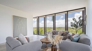 A modern living room with a large window, grey sofas, and a wooden coffee table with a vase. - Unique unit, private pool, terrace, views! (Tulum)