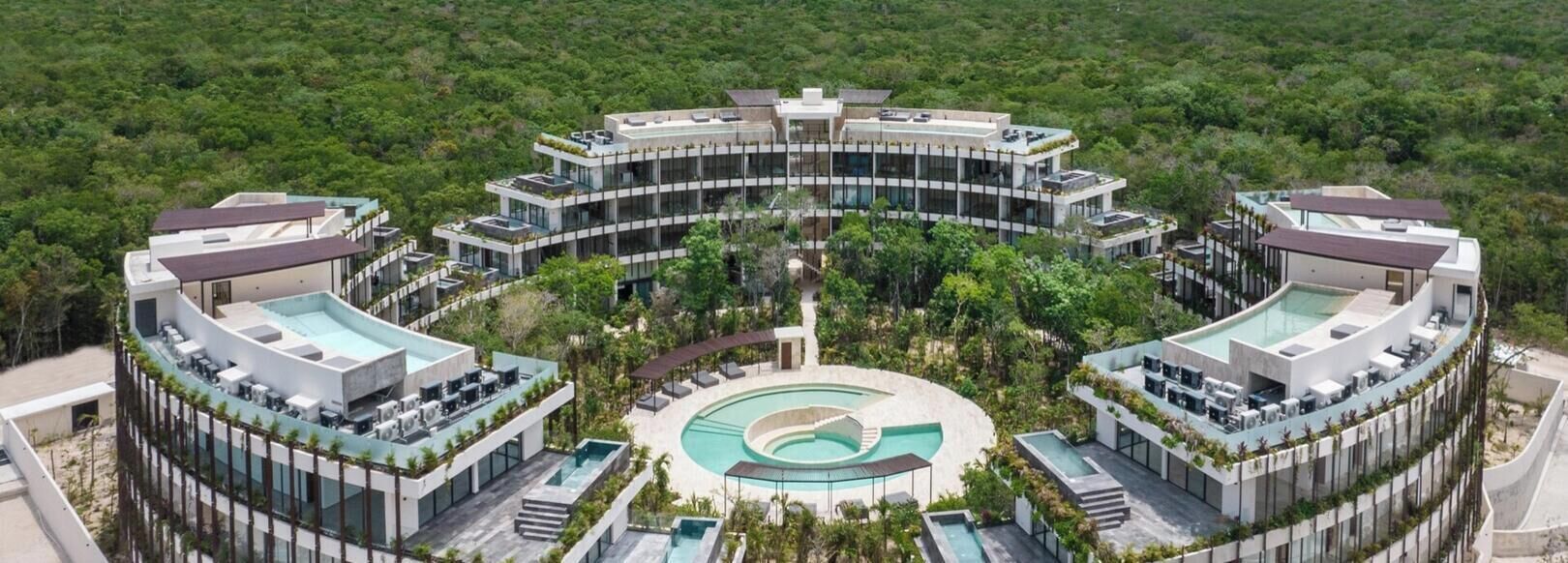 Ein modernes Hotel mit zentralem Pool, umgeben von üppiger Vegetation und freiem Blick auf den Ozean.