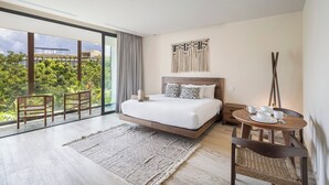 A modern hotel room with a large bed, a dining table, and a view of lush greenery. - Bright and Cozy Studio with Pool View – Perfect for Couples (Tulum)