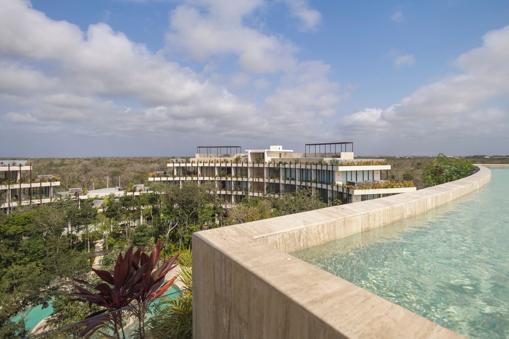 Un complexe hôtelier moderne doté d’une piscine, d’une végétation luxuriante et offrant une vue dégagée sur l’océan.