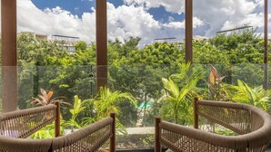 A glass-enclosed outdoor seating area with wicker chairs, surrounded by lush greenery and a clear sky. - Bright and Cozy Studio with Pool View – Perfect for Couples (Tulum)
