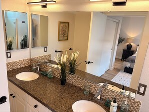 Une salle de bain avec deux lavabos, un grand miroir et une plante en pot.
