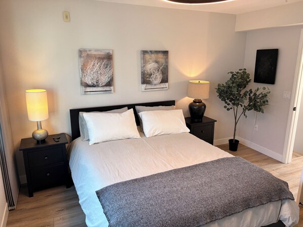 Une chambre à coucher comprenant un lit, deux tables de chevet, une lampe, une plante en pot et deux œuvres d’art murales.