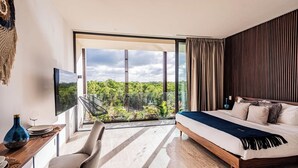 Een moderne slaapkamer met een groot bed, een bureau met stoel, en een balkon met uitzicht op groen.