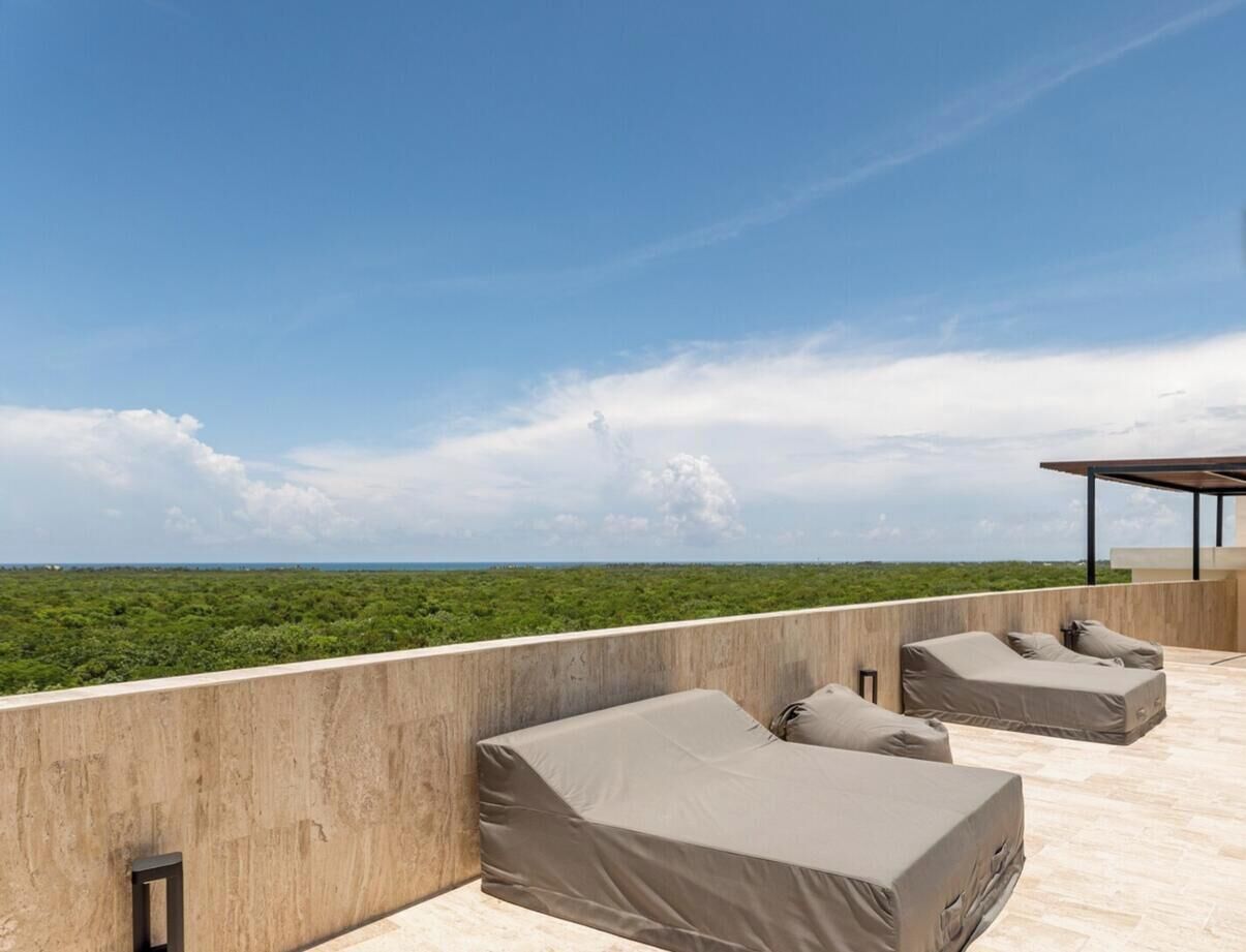 A rooftop terrace with two sun loungers and a covered seating area, overlooking a green landscape.