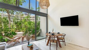 Quarto moderno com uma grande parede de vidro, uma mesa de jantar com cadeiras, uma TV fixada na parede e uma rede do lado de fora.