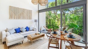 Uma sala de estar moderna com sofá, mesa de centro e mesa de jantar, grandes janelas com vista para o verde.
