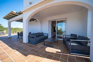 A covered outdoor seating area with a sofa, chairs, and a coffee table. - Villa Finesse tipo 2 (Son Bou)