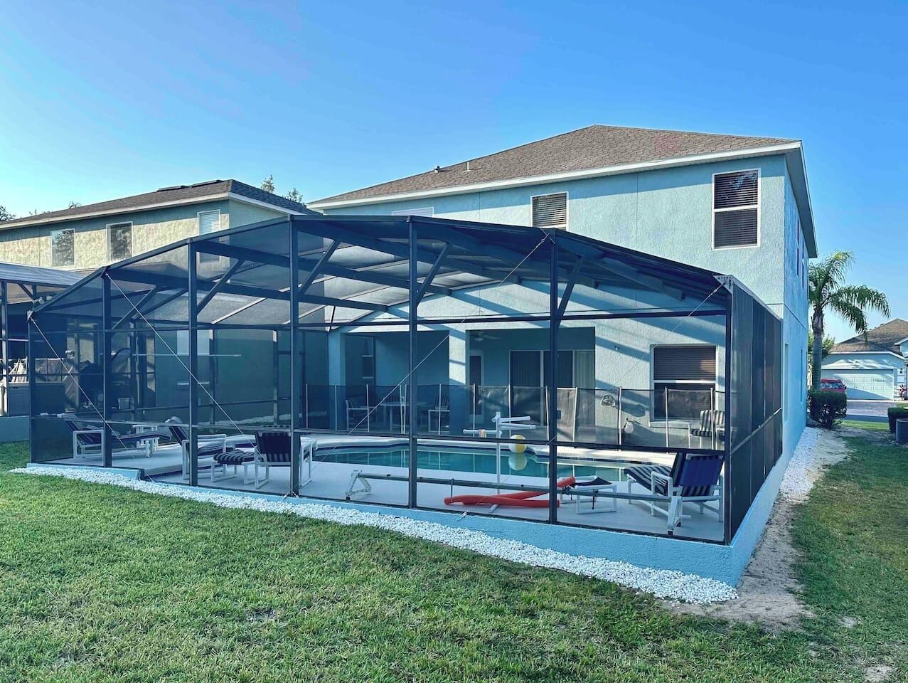 Une maison moderne dotée d’un patio entièrement vitré, comprenant une piscine, du mobilier d’extérieur et offrant une vue dégagée sur l’intérieur.