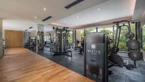 Une salle de sport moderne dotée d’un plancher en bois, de murs recouverts de miroirs et de divers équipements d’exercice, notamment une pile de poids portant l’inscription « MISTIQ TULUM ».