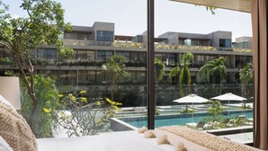 Une chambre d’hôtel moderne dotée d’une grande fenêtre donnant sur une piscine et un jardin aménagé.