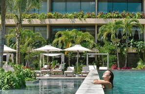 A pool area with lounge chairs and umbrellas, surrounded by lush greenery and a modern building facade. - Marvellous Modern Studio with balcony (Tulum)