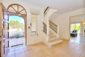 Un vestíbulo amplio con una escalera blanca, una puerta que da al exterior y vistas al paisaje.