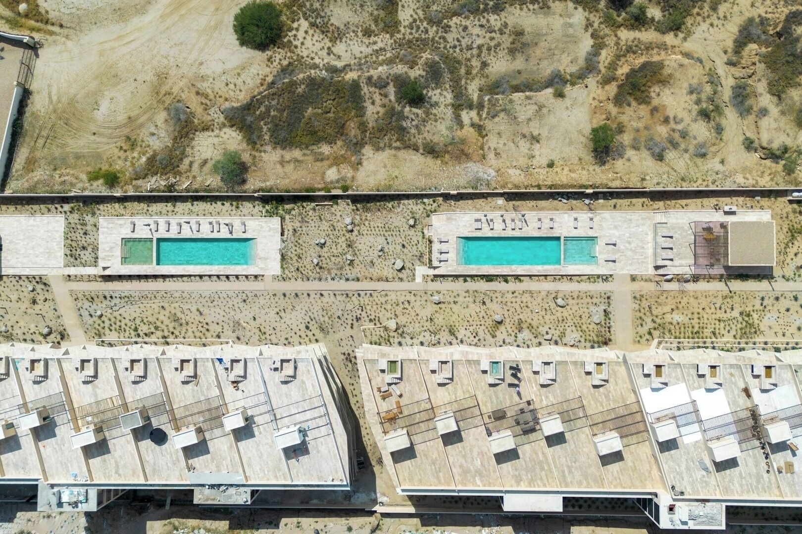 Vue aérienne d’un complexe hôtelier doté de plusieurs piscines, d’un parking et, en arrière-plan, d’un paysage désertique.