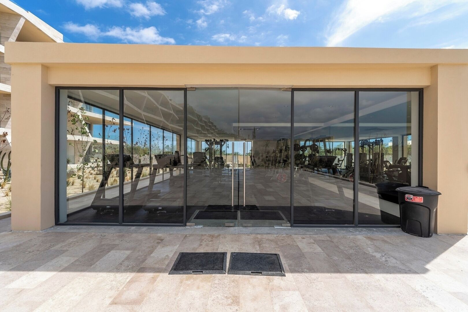 A modern building with large glass doors, a paved entrance area, and outdoor exercise equipment visible through the glass.