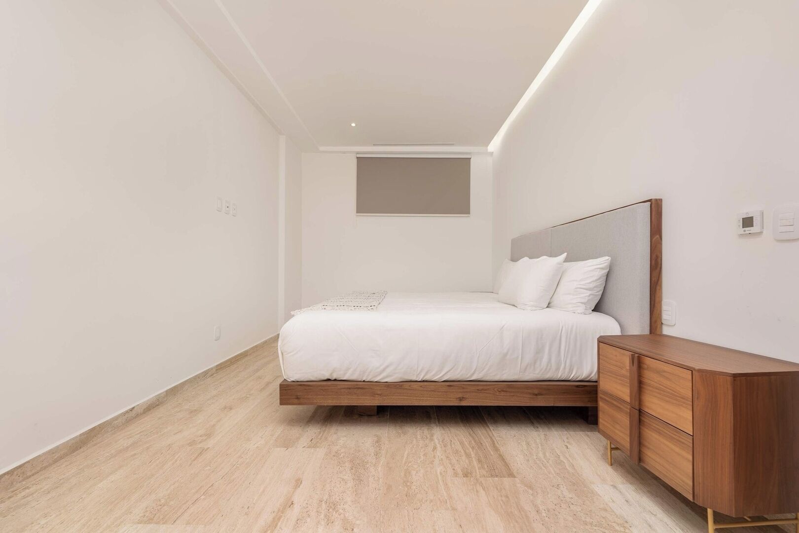 A minimalist bedroom with a bed, wooden bedside tables, and a small window.