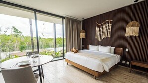 Une chambre moderne avec un grand lit, une table à manger et une vue sur la verdure environnante.