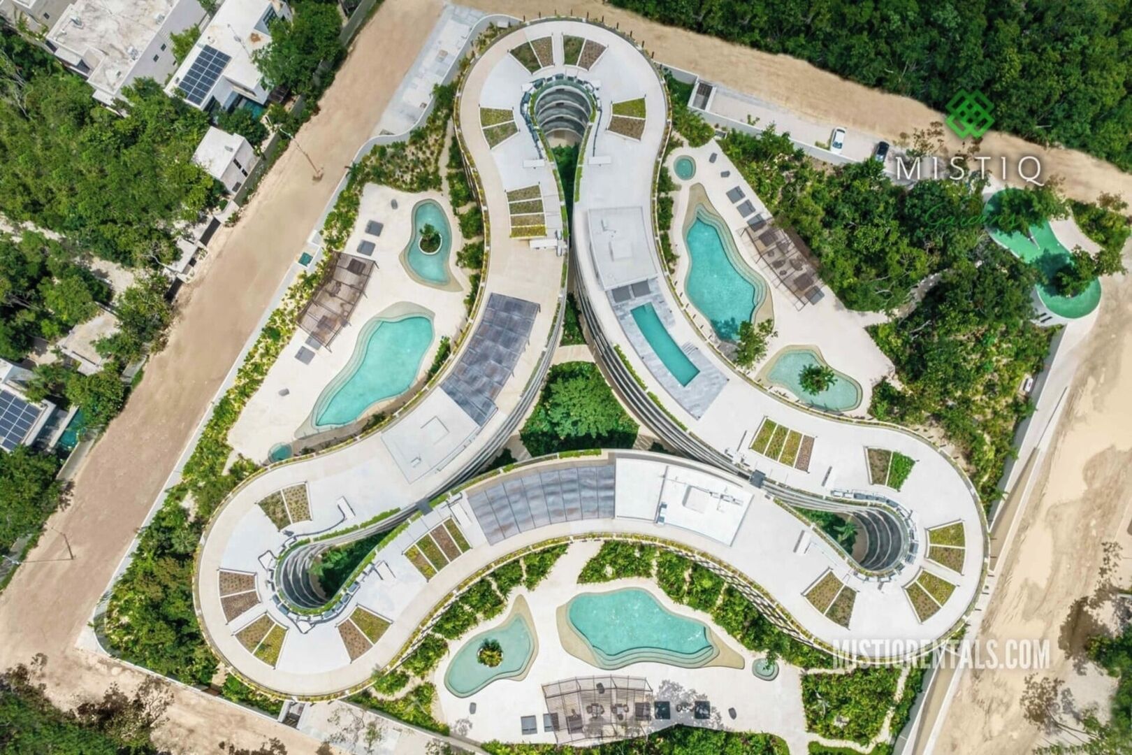 Vista aérea de un complejo turístico con piscinas interconectadas, un edificio central y follaje circundante.