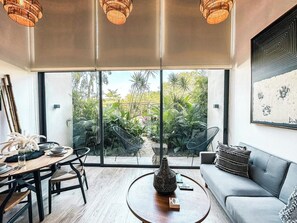 Ein modernes Wohnzimmer mit Essbereich, großen Fenstern und Blick auf tropische Pflanzen.