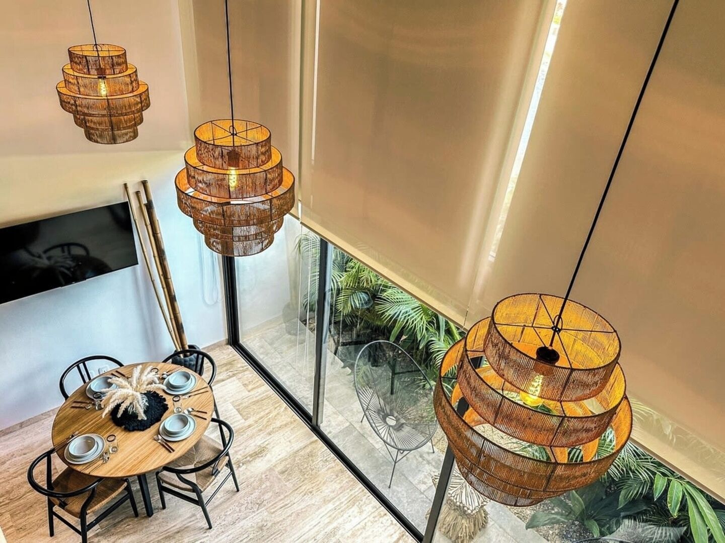 Een eethoek met een ronde houten tafel, zwarte stoelen en een hangende houten lamp.