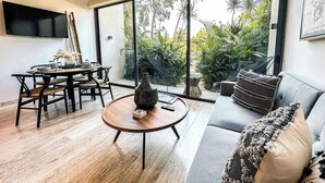 A modern living room with a dining area, large windows, and a view of greenery outside. - Astounding Loft with Gym, Pool and Beach Shuttle (Tulum)