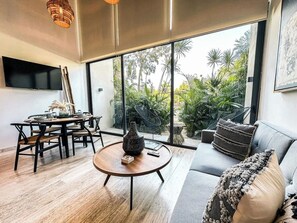 Ein modernes Wohnzimmer mit Essbereich, großen Fenstern und Blick auf Grünfläche.
