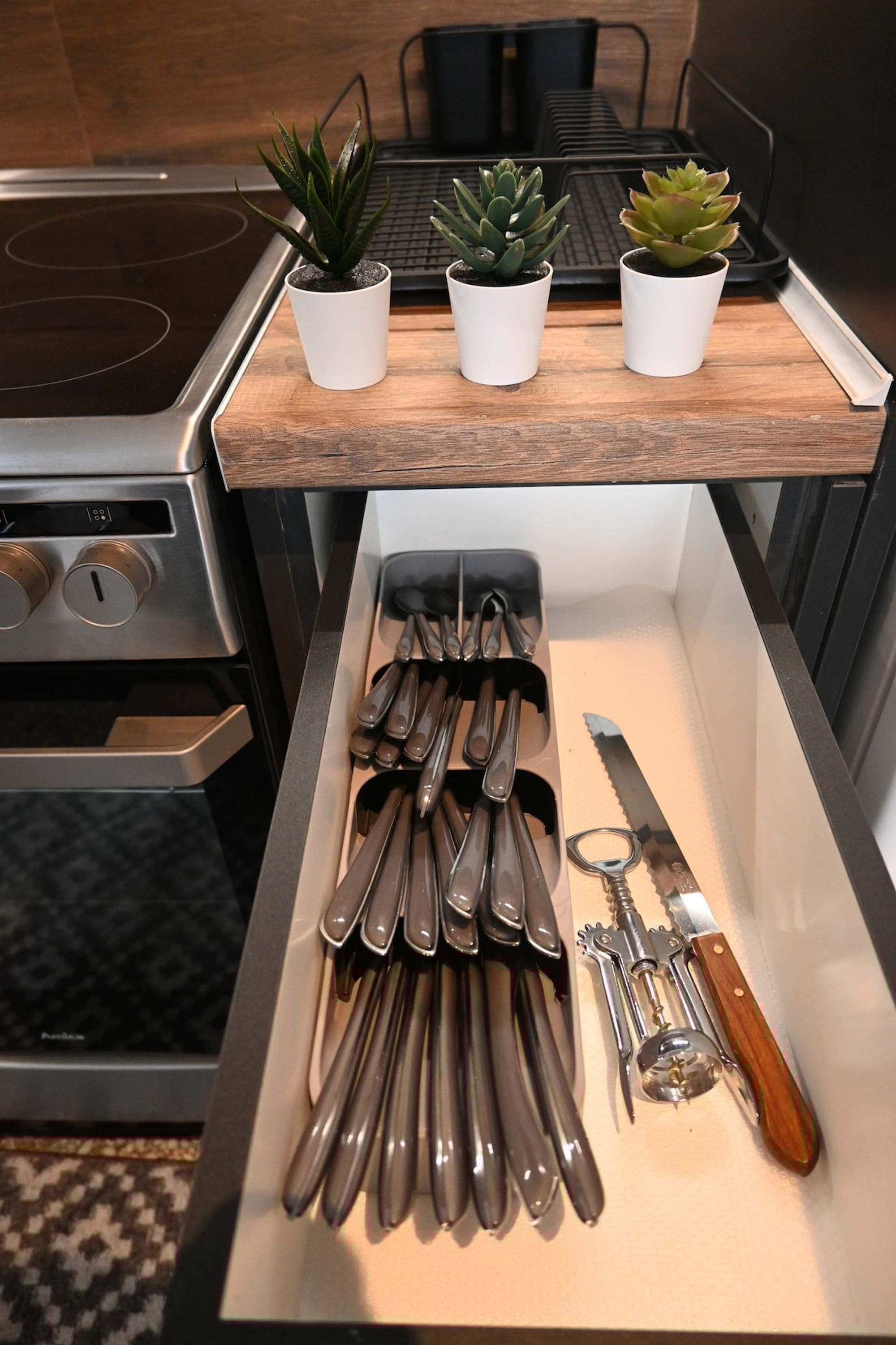 Una encimera de cocina con tres suculentas en macetas y un cajón con utensilios de cocina.