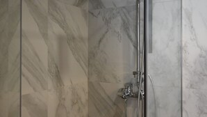 Une douche moderne dotée d’un pommeau de douche à main et d’un robinet mural, le tout installé sur un mur recouvert de carreaux de marbre.
