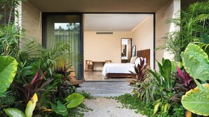 A modern hotel room with a bed, a desk, and a chair, and a view of the garden through the glass door. - Cozy Std, Steps to Infinity Pool, Shuttle to Beach (Tulum)