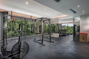 A modern gym with various exercise equipment, large windows, and a view of greenery. - Cozy Std, Steps to Infinity Pool, Shuttle to Beach (Tulum)