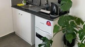 A compact kitchen with white cabinets, a black countertop, a coffee maker, and a potted plant. - Urban Hermes Apartment (Athina)