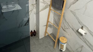 A bathroom with a glass shower enclosure, a wooden ladder, a bucket, and a toilet paper holder. - Urban Hermes Apartment (Athina)