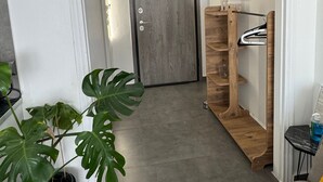 A hallway with a wooden door, a potted plant, a wooden shelf unit, and a small table with a bottle. - Urban Hermes Apartment (Athina)