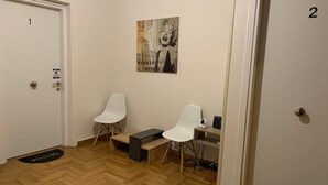 Eine Hotelhalle mit zwei weißen Stühlen, einem kleinen Tisch, einer Fußmatte und einem Wandbild.