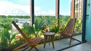 Un balcón con dos sillas de madera y una pequeña mesa, con vistas a un paisaje verde y exuberante y edificios a lo lejos.