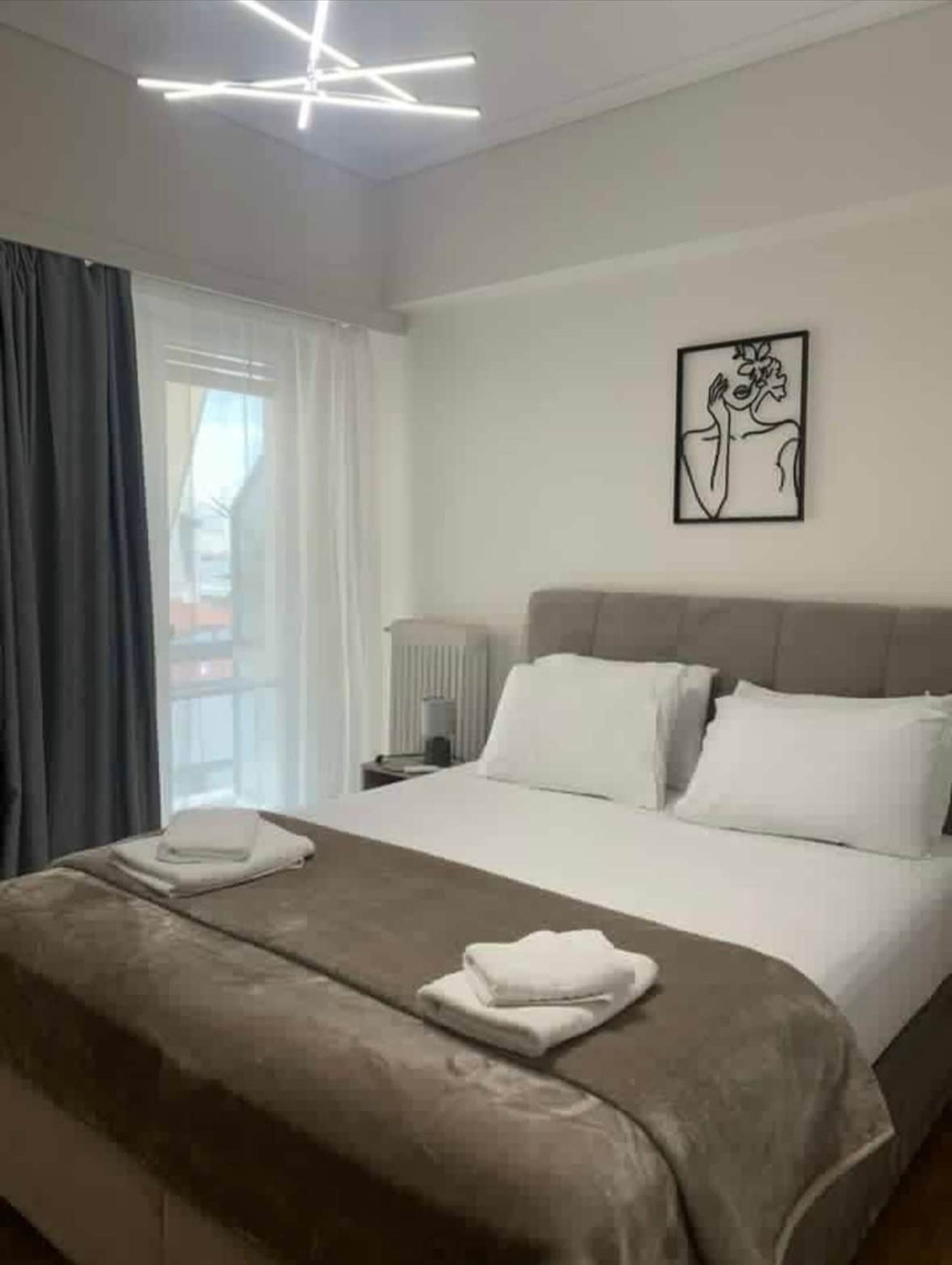 Una habitación de hotel con una cama grande, una mesita de noche, una lámpara y una ventana con cortinas.