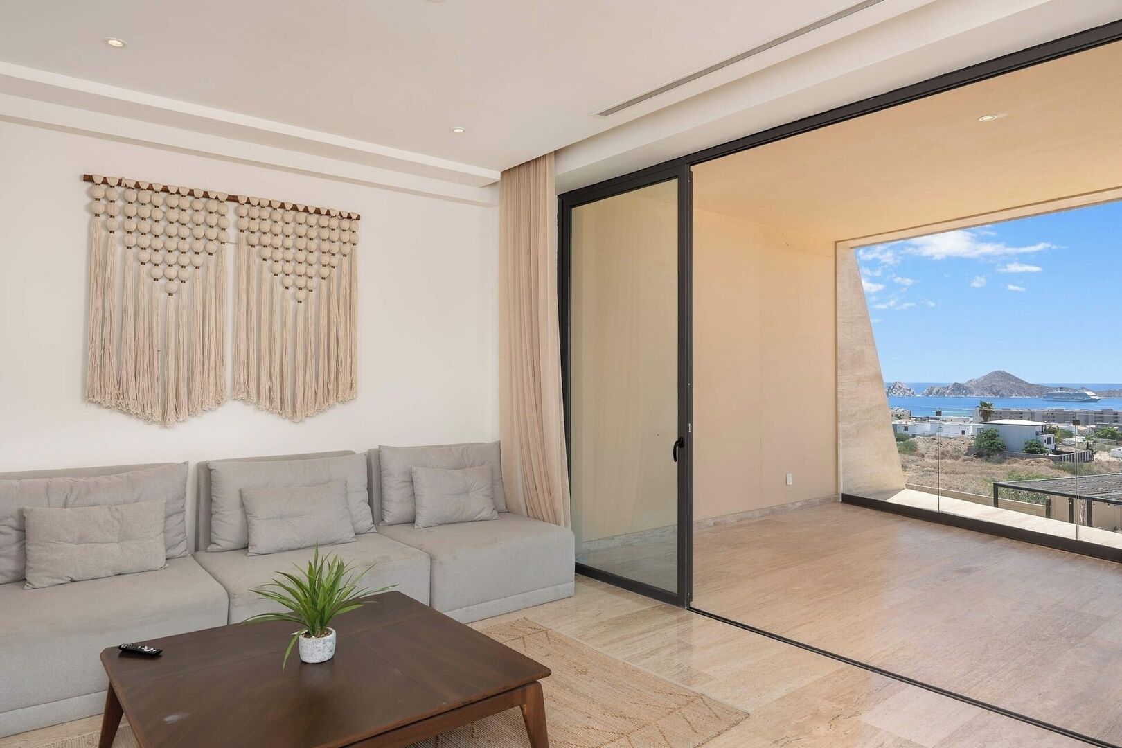 A modern living room with a sofa, a coffee table, and a view of the sea through a large sliding glass door.