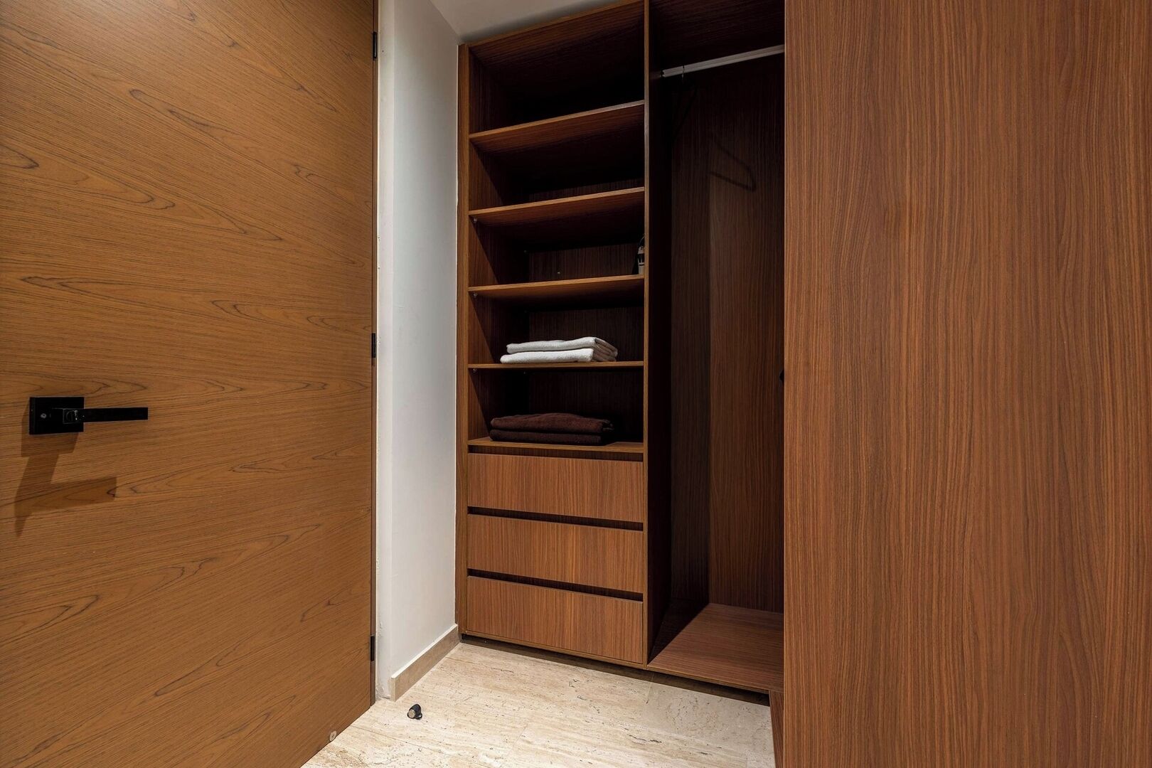 Ein Holzschrank mit mehreren Regalen und Schubladen, ein kleines schwarzes Objekt auf dem Boden und eine weiße Wand.