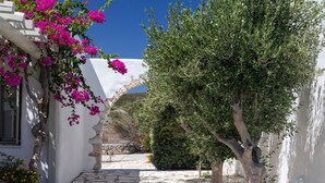 A narrow stone-paved courtyard with a white building, a tree, and bougainvillea flowers. - Villa Santa Bliss Paros (Paros)