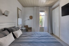 Une chambre à coucher avec un grand lit, un bureau, une chaise, une télévision et une fenêtre avec des rideaux.